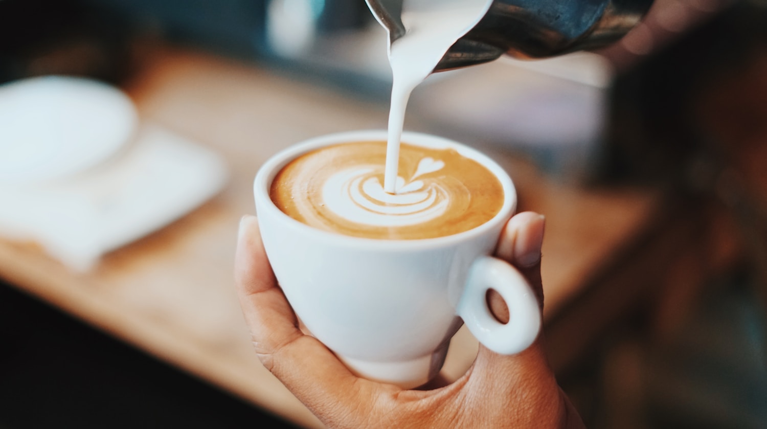 Manos de un barista vertiendo leche y dibujando latte art en una taza de café